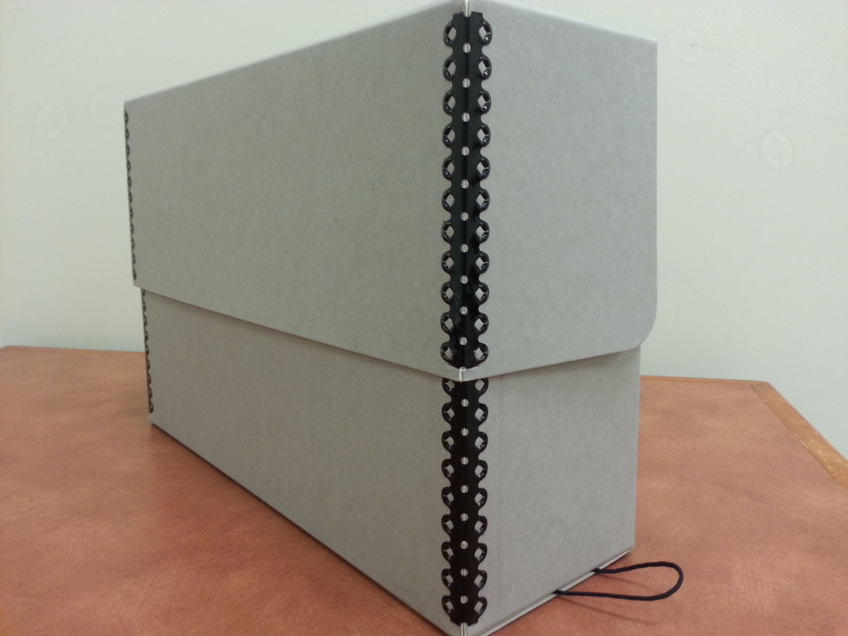 A gray archival document box with metal-edge corners resting on a warm brown surface.
