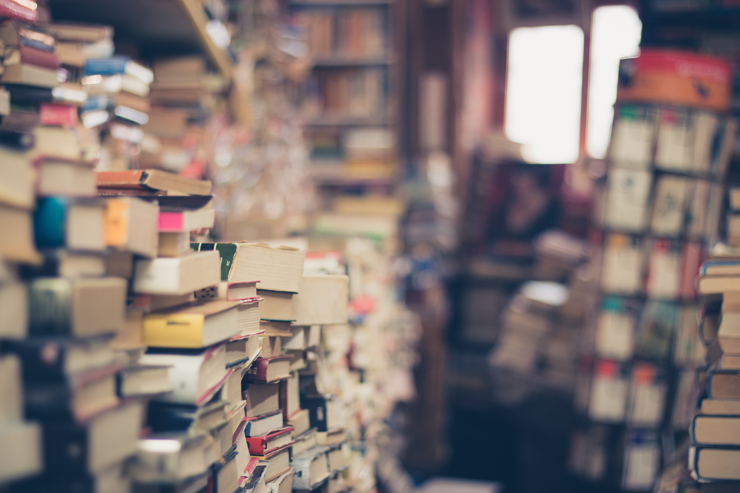 Worn books stacked beside a softly lit aisle in a secondhand bookshop.